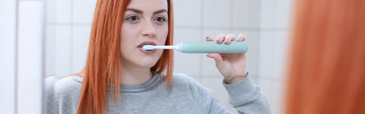 Woman brushing her teeth in front of a mirror.