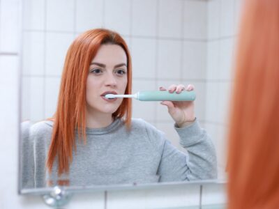 Woman brushing her teeth in front of a mirror.