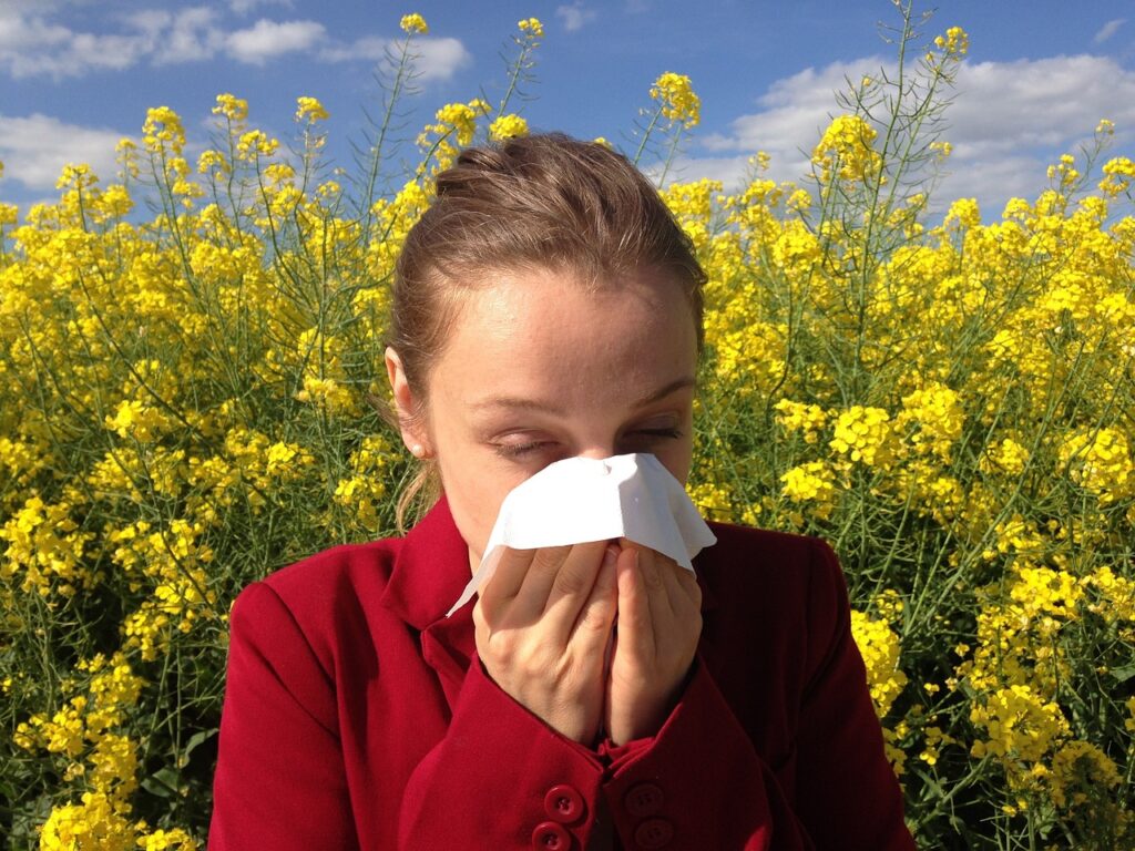 A women surrounded by flowers blowing her nose.