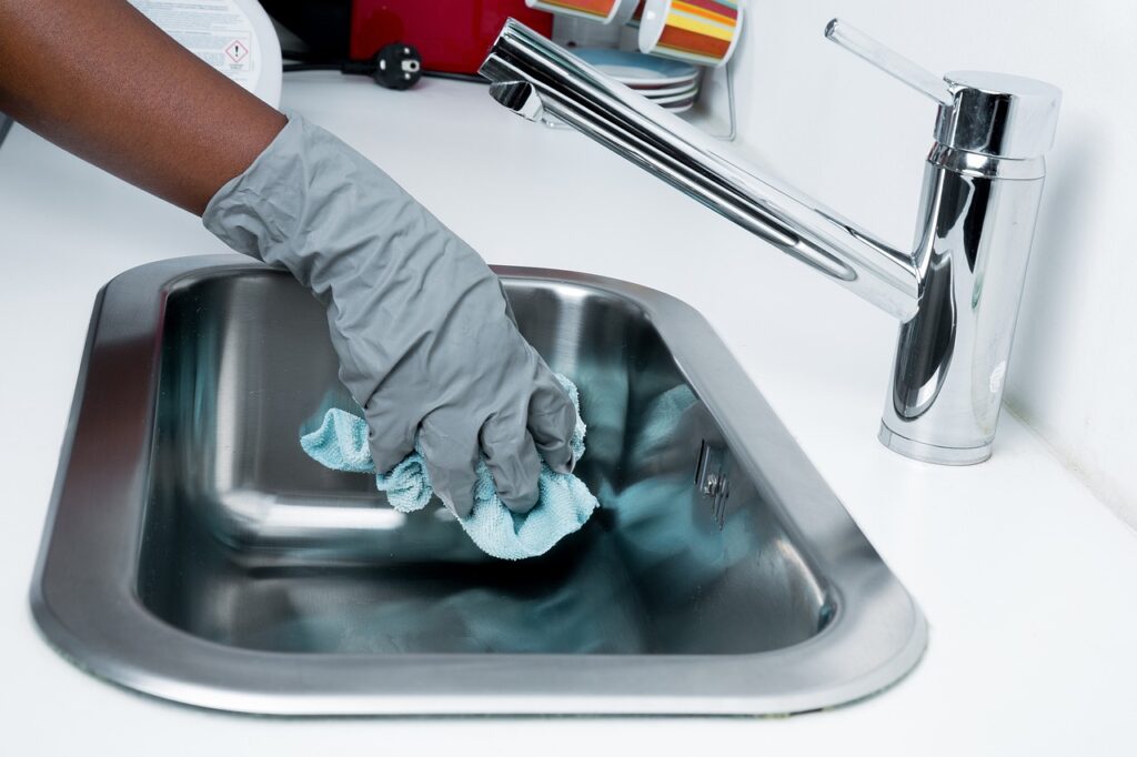 gloved hand using rag to clean silver sink.