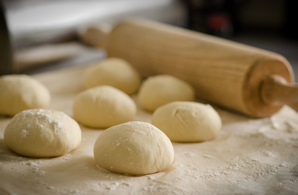 Mounds of dough and a roller sitting on a table. 