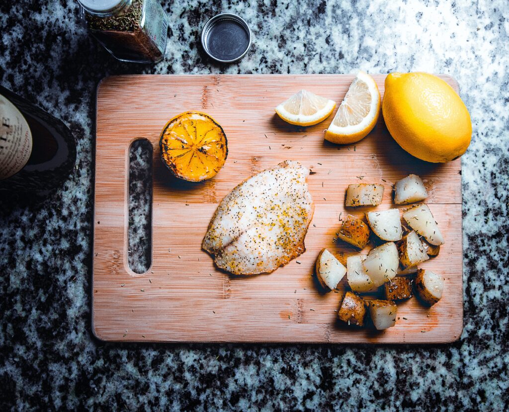 Cooked fish, potatoes, and lemons on a cutting board. 