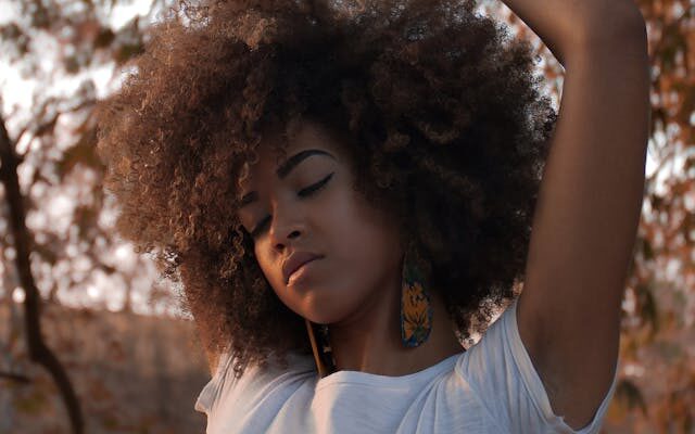 Black woman with type 4 hair posing in front of fall scenery.