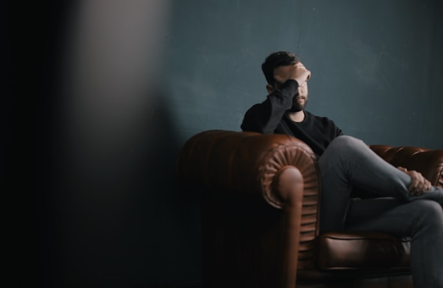 Man in chair with hand covering face. Image featured in World Mental Health Day article.