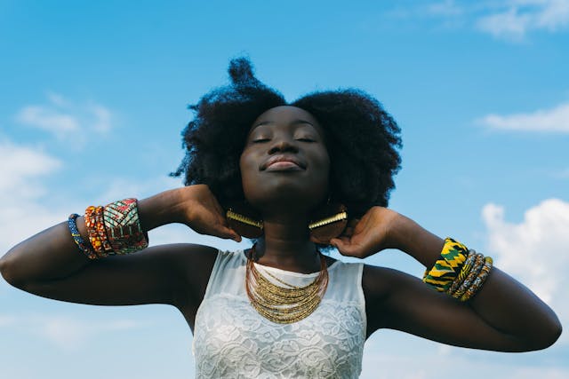 Black woman with type 4 hair posing with the background of the sky.