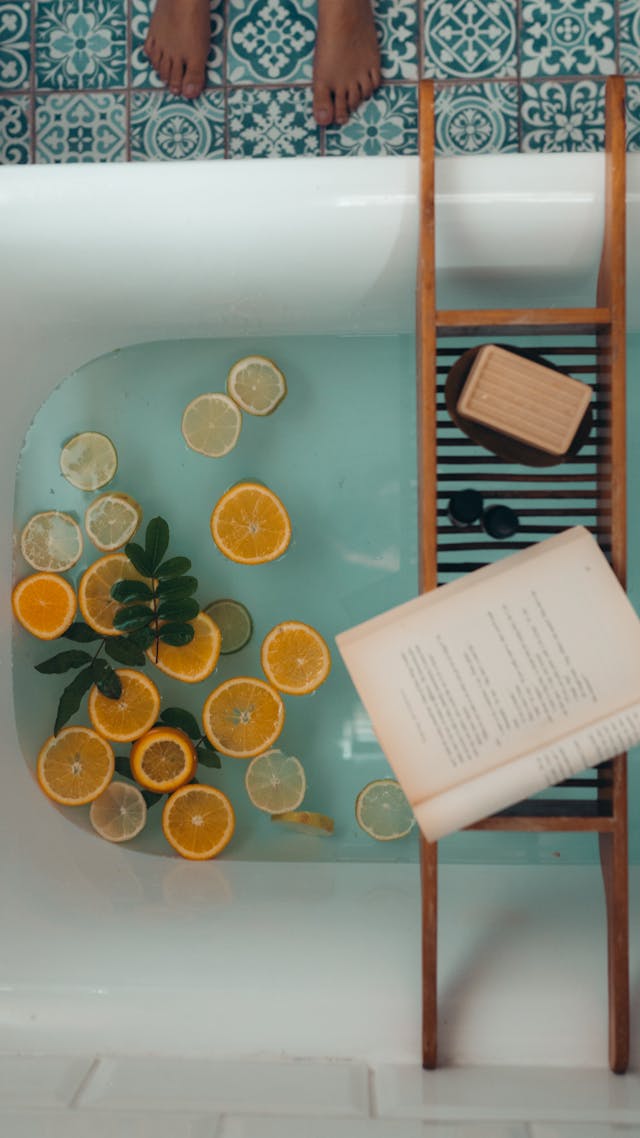 Bath with lemons in it, with soap and a book on a stool for self care.