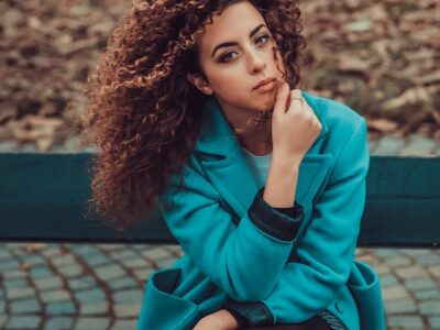 Woman with type 3 hair sitting wearing teal jacket.