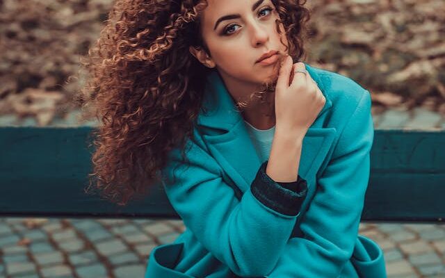 Woman with type 3 hair sitting wearing teal jacket.