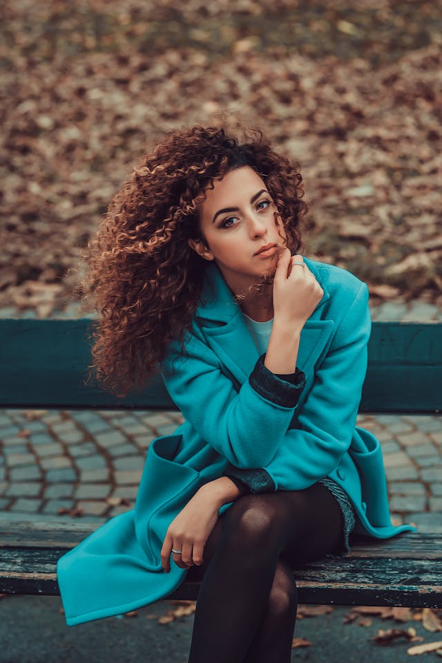 Woman with type 3 hair sitting wearing teal jacket.