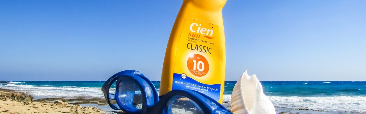 Sunscreen in the sand next to a pair of swim goggles.