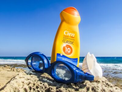 Sunscreen in the sand next to a pair of swim goggles.