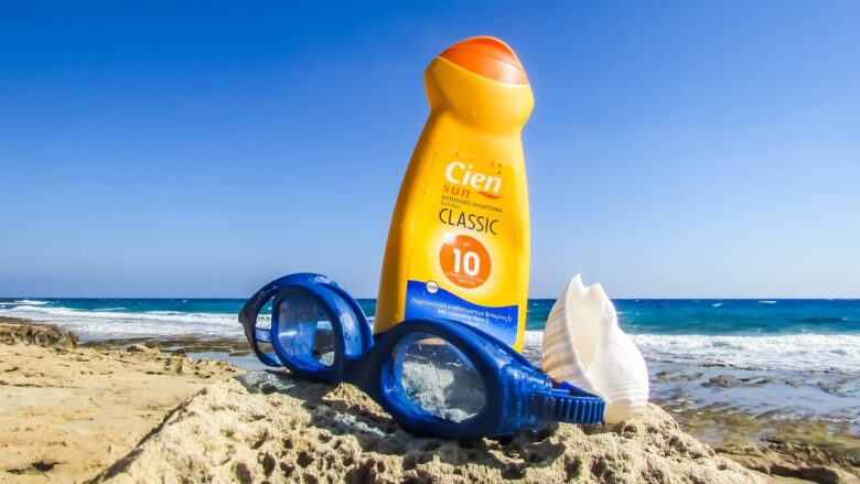 Sunscreen in the sand next to a pair of swim goggles.