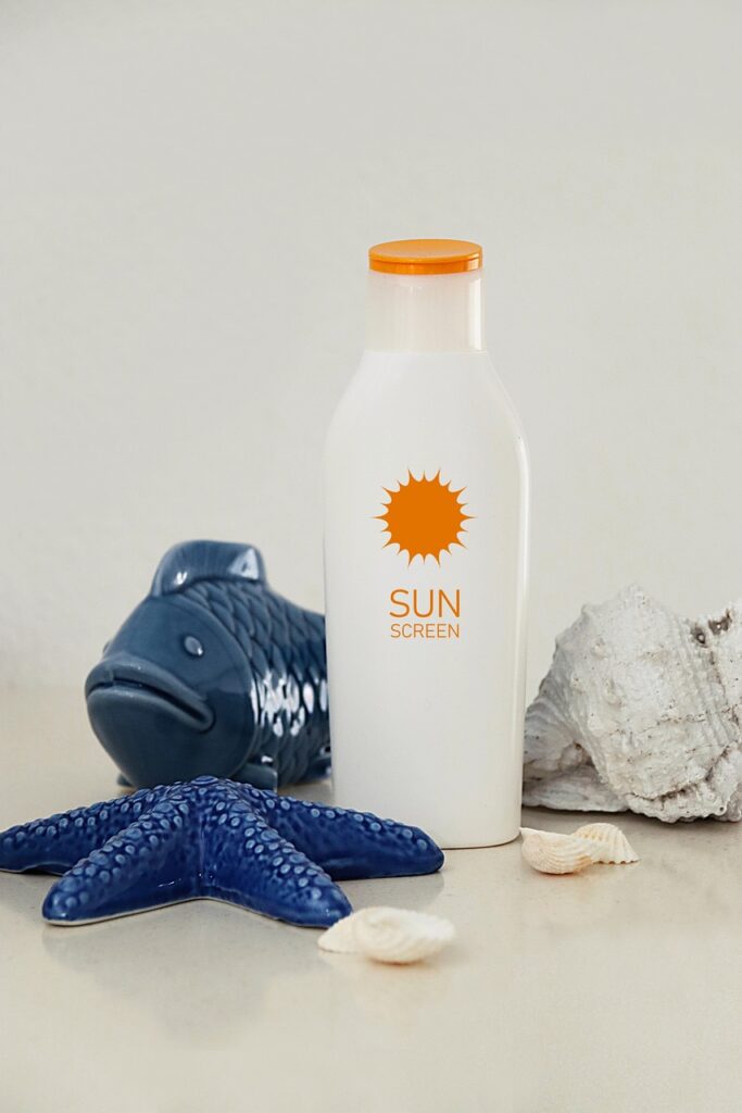 Sunscreen surrounded by seashells, a glass blue starfish and a glass blue fish.