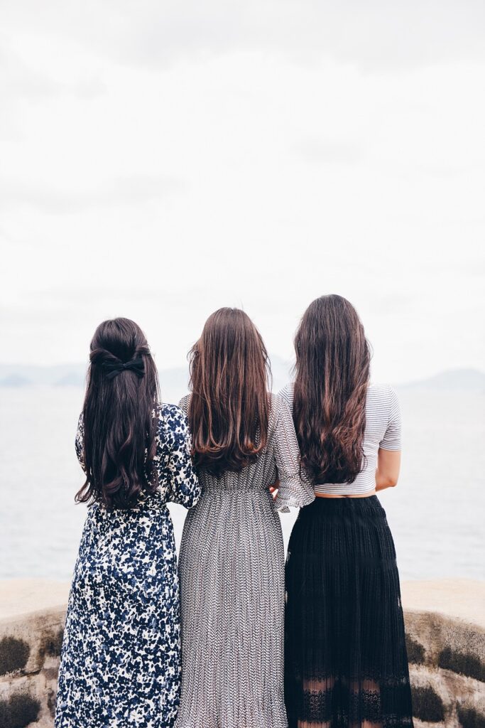 Three women with their hair out facing the water.