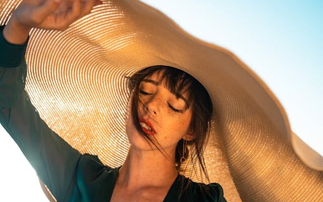 Woman with brown colored sun hat and green shirt standing in front of the sky.