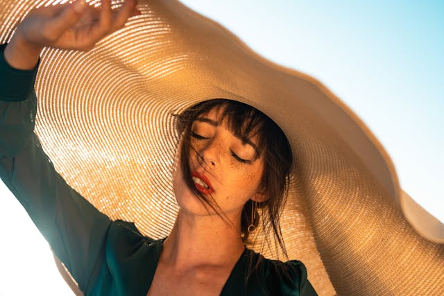 Woman with brown colored sun hat and green shirt standing in front of the sky.