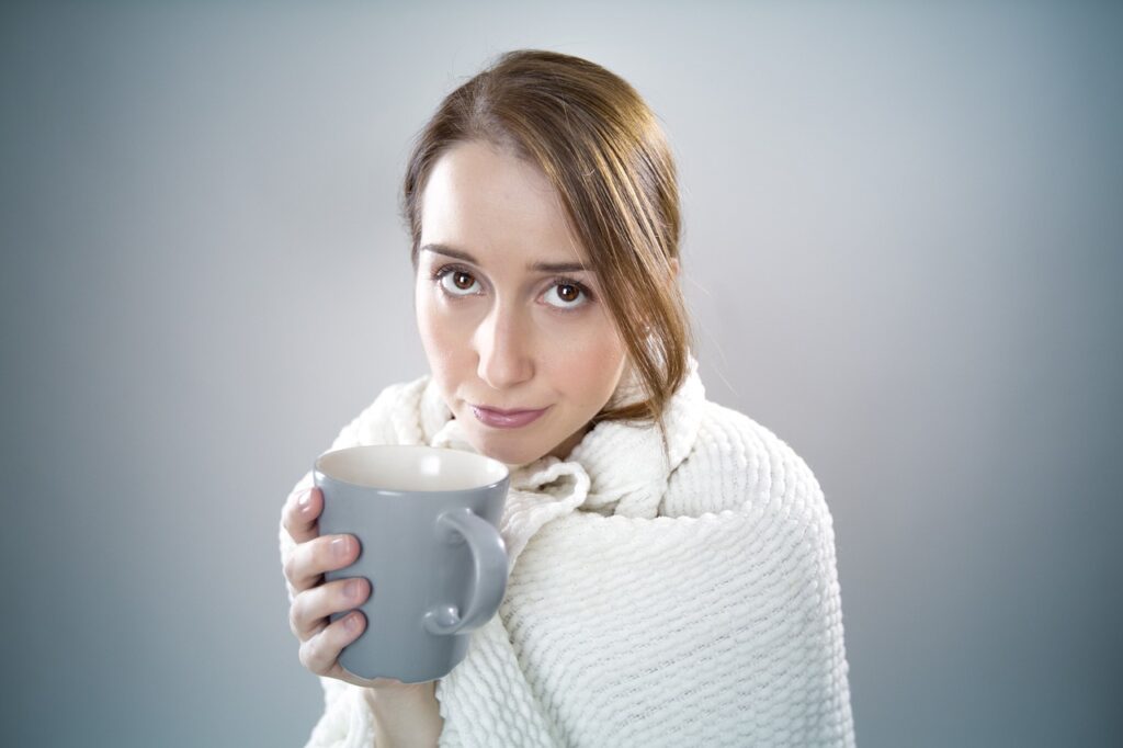 A woman wrapped in a blanket and holding a mug.